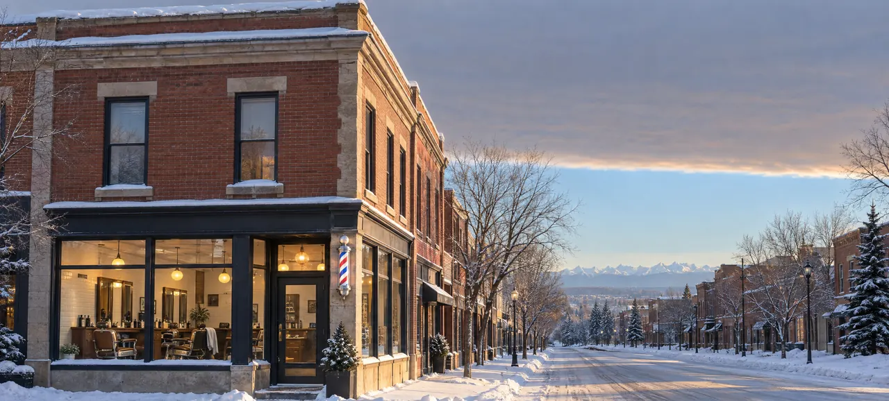 A corner barbershop in an old brick block on a snowy Calgary street just after sunrise, its windows lit under a chinook arch